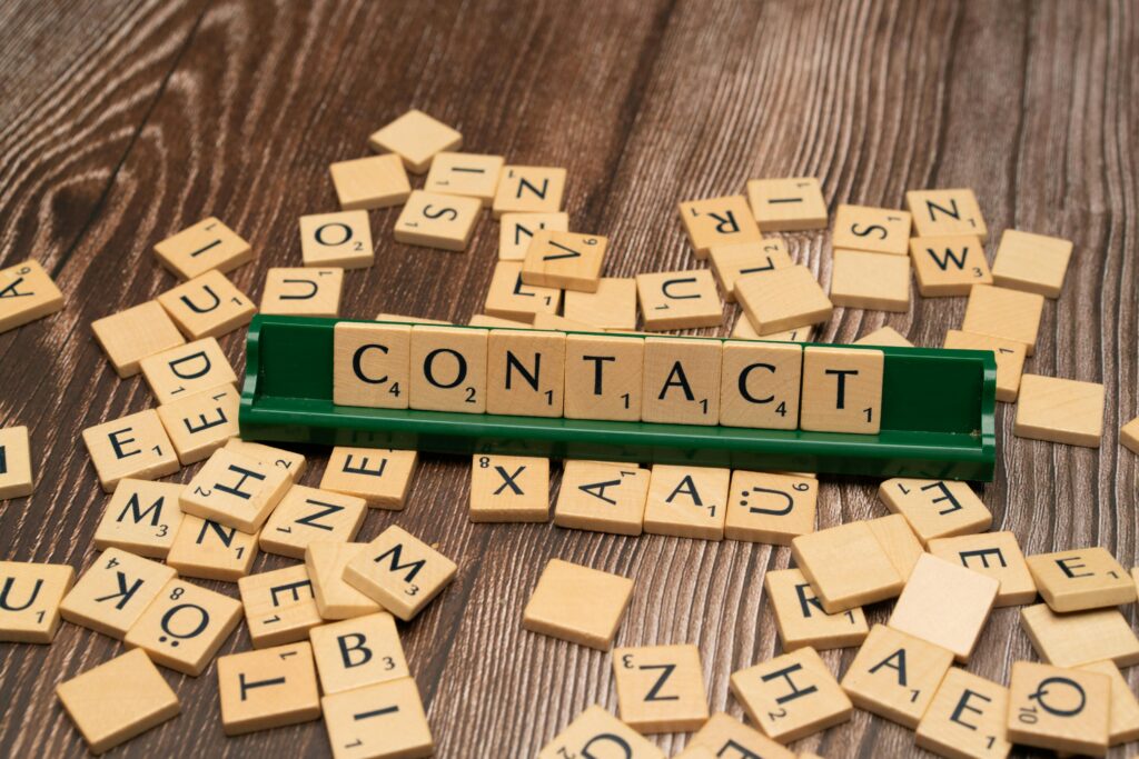 Scrabble tiles spelling 'CONTACT' on a wooden surface with scattered tiles around.