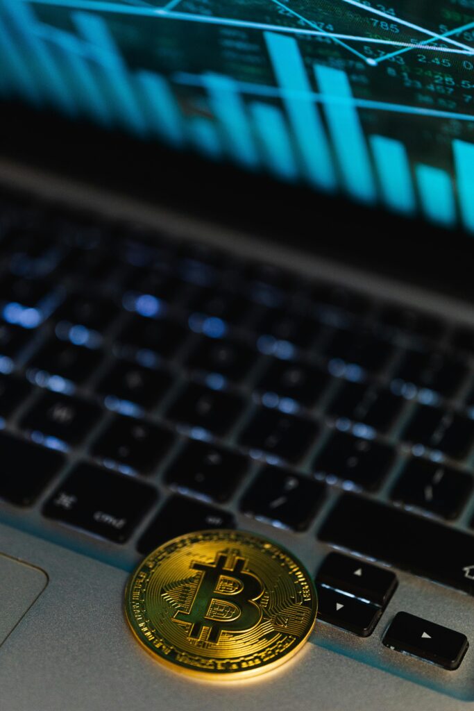 Gold Bitcoin coin on a laptop keyboard with trading chart display.