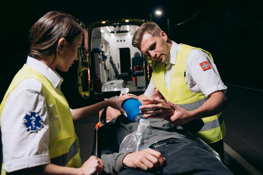 Two paramedics perform first aid on a patient at night by an ambulance.